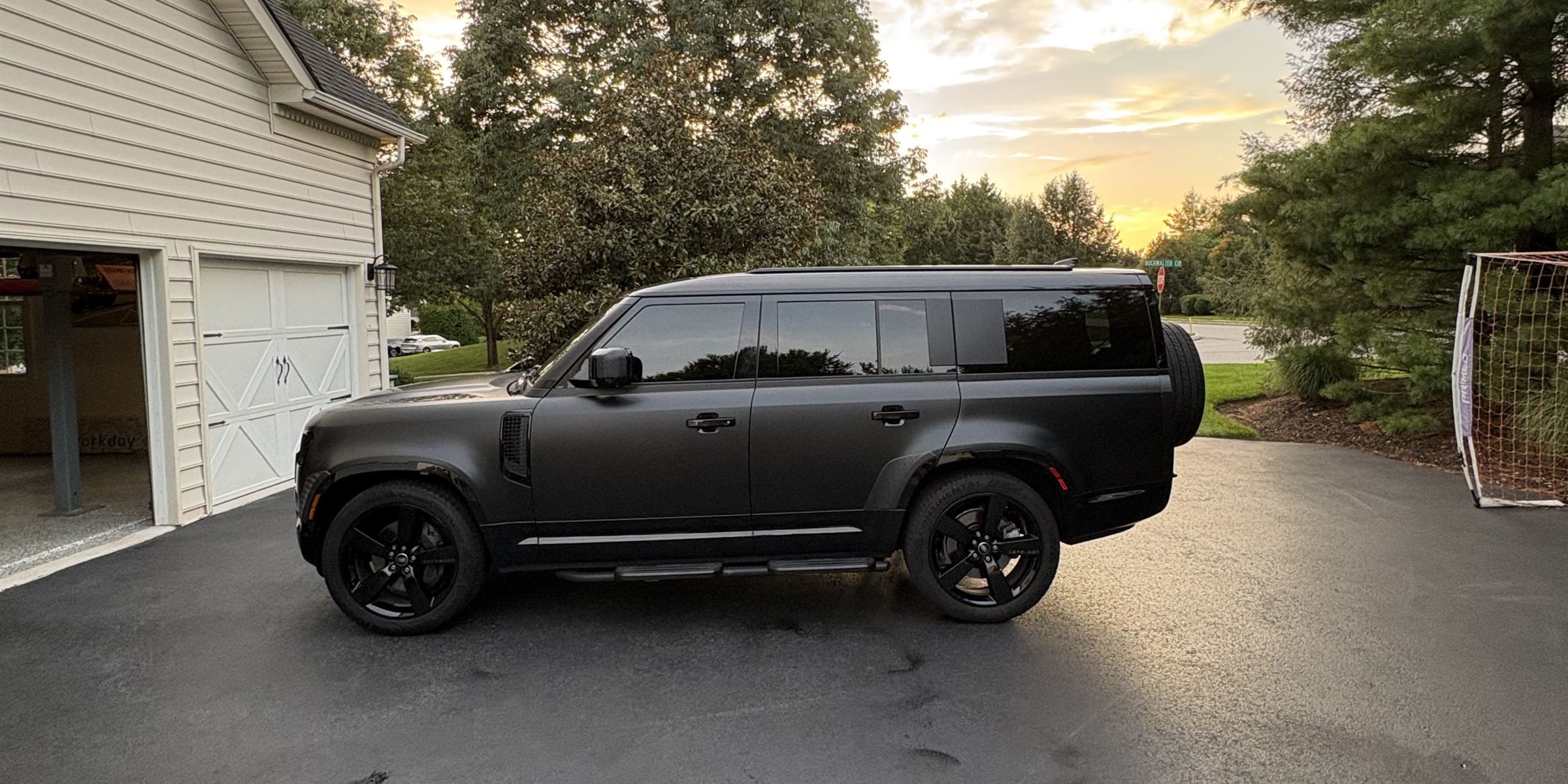 A matte black Land Rover Defender finished in a residential driveway at sunset