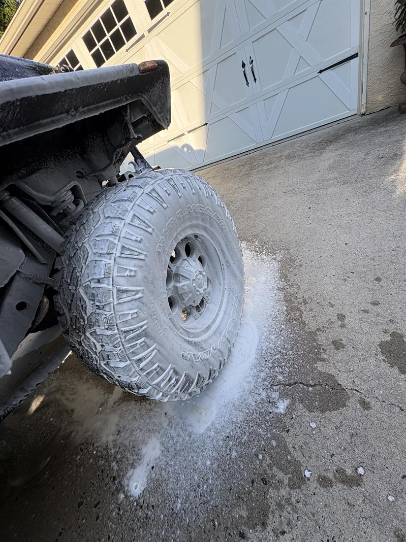 A wheel covered in cleaning foam with suds running onto the driveway